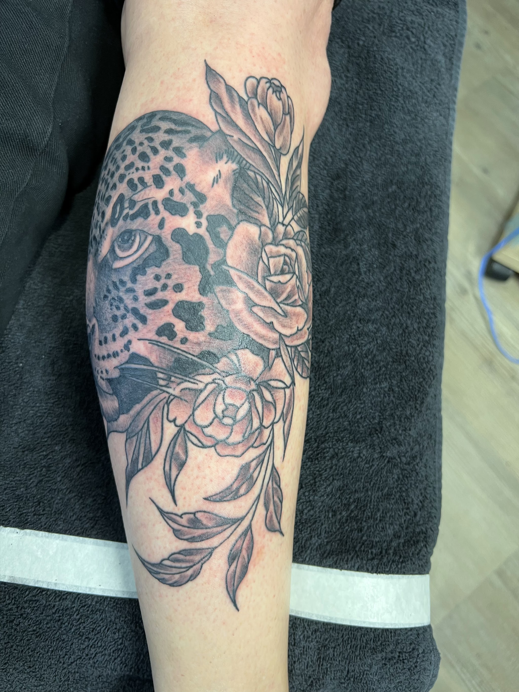 Afgewerkte zwart-grijze tatoeage van een luipaard met bloemen op een been